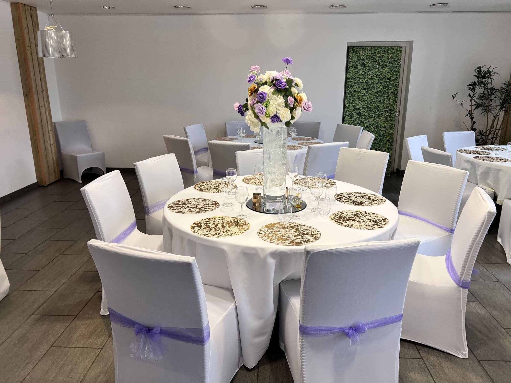 Table d'invités lilas et doré, housses à nœuds mauves et haute composition de roses blanches, mariage à Épône