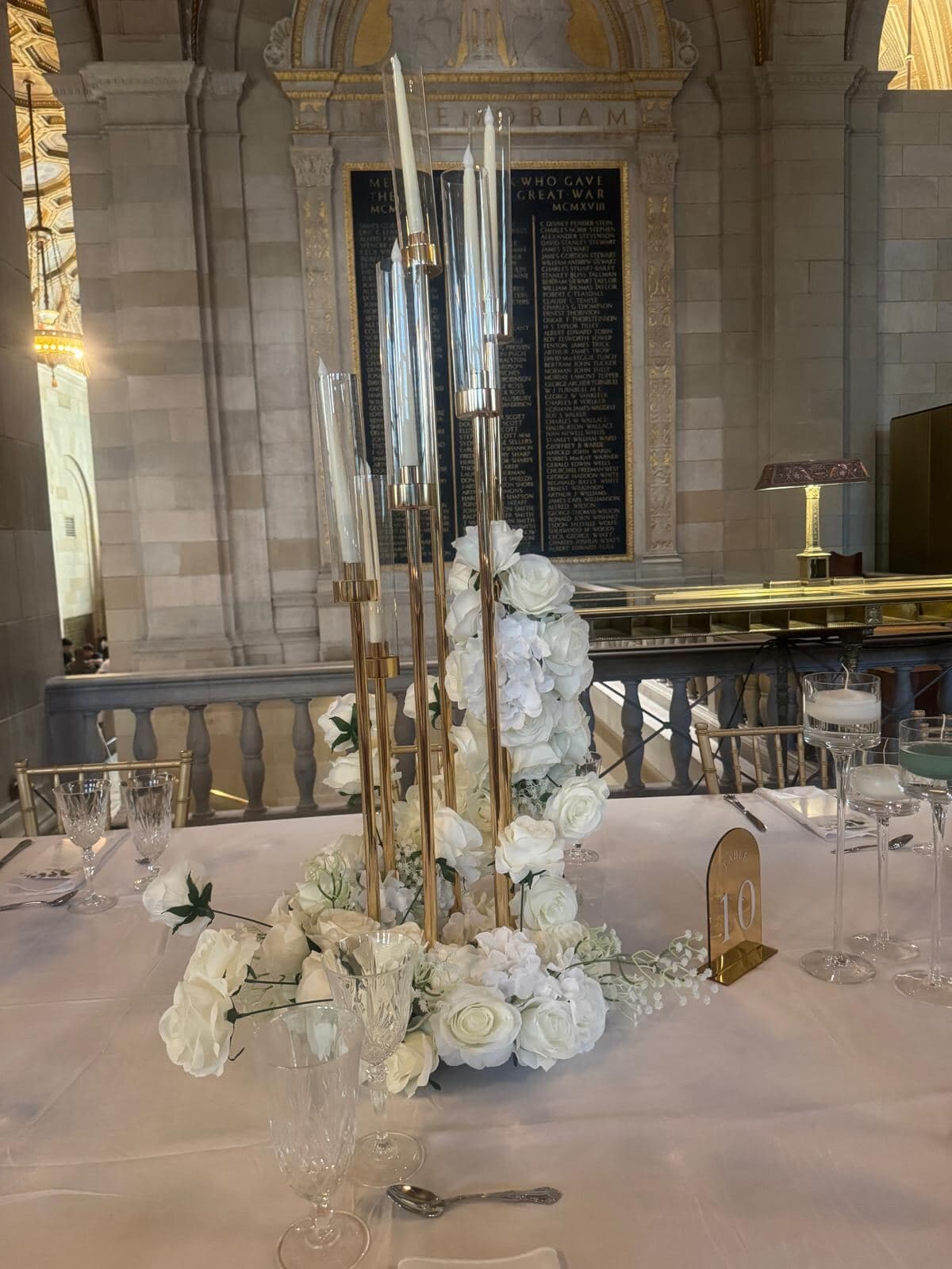 Centre de table : candélabre doré et colonne de roses blanches sous les voûtes de pierre, Montréal